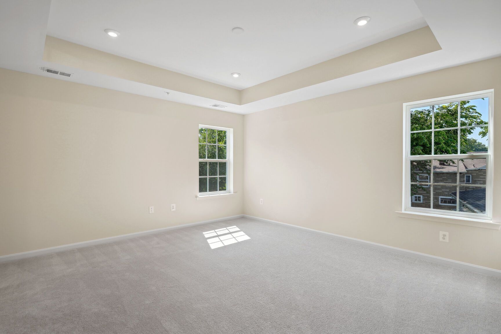 An empty bedroom with two windows and a carpeted floor.
