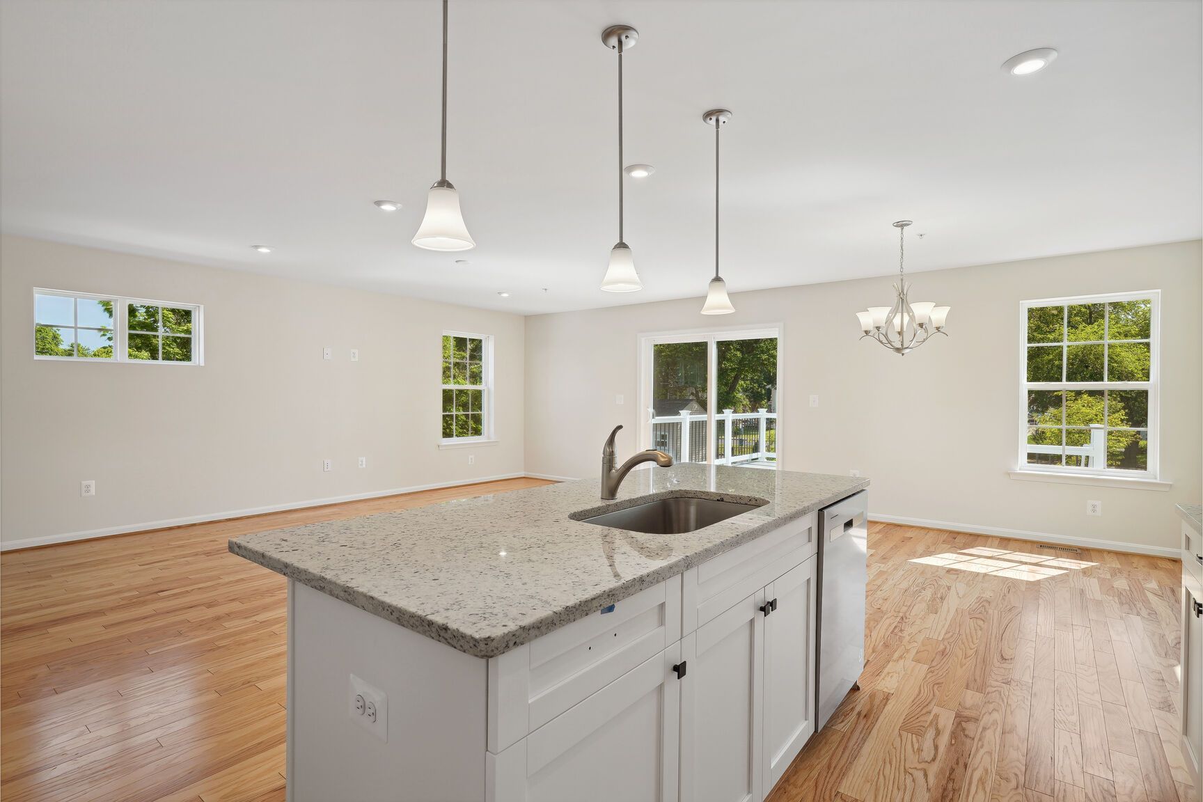 An empty kitchen with a large island and granite counter tops.