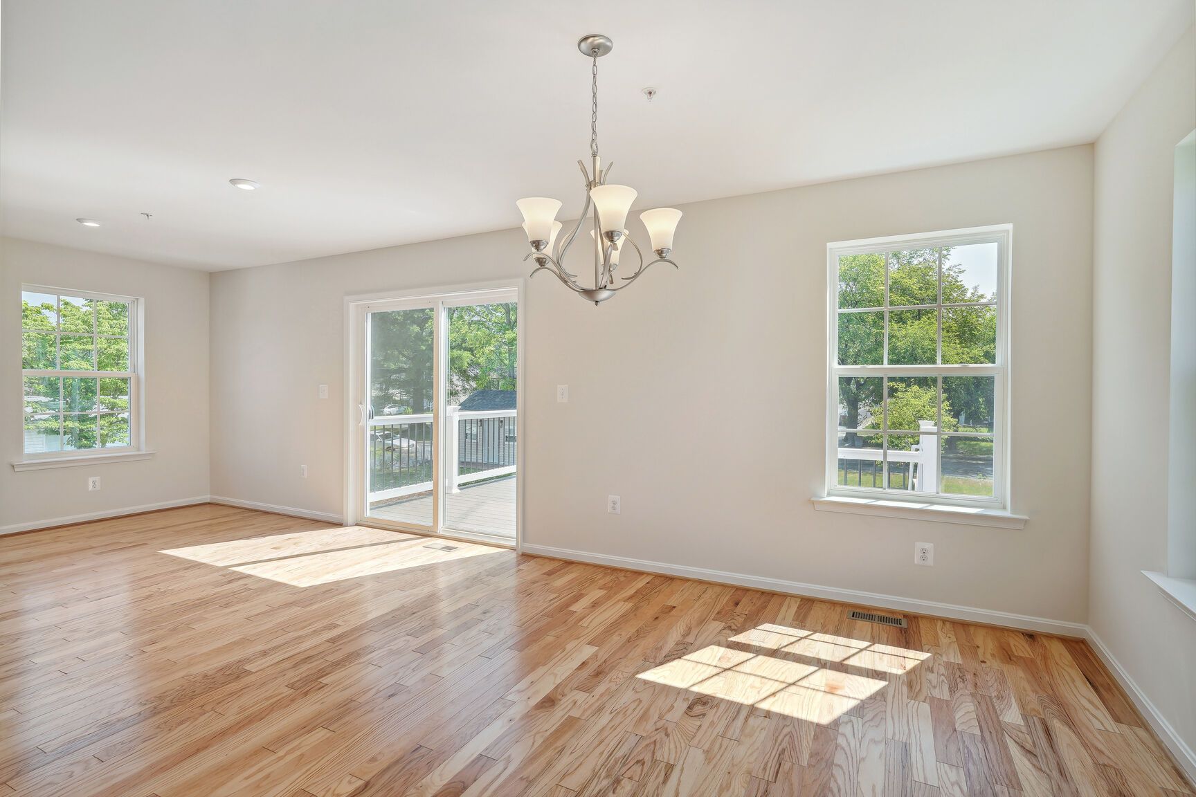 An empty living room with hardwood floors and a chandelier.