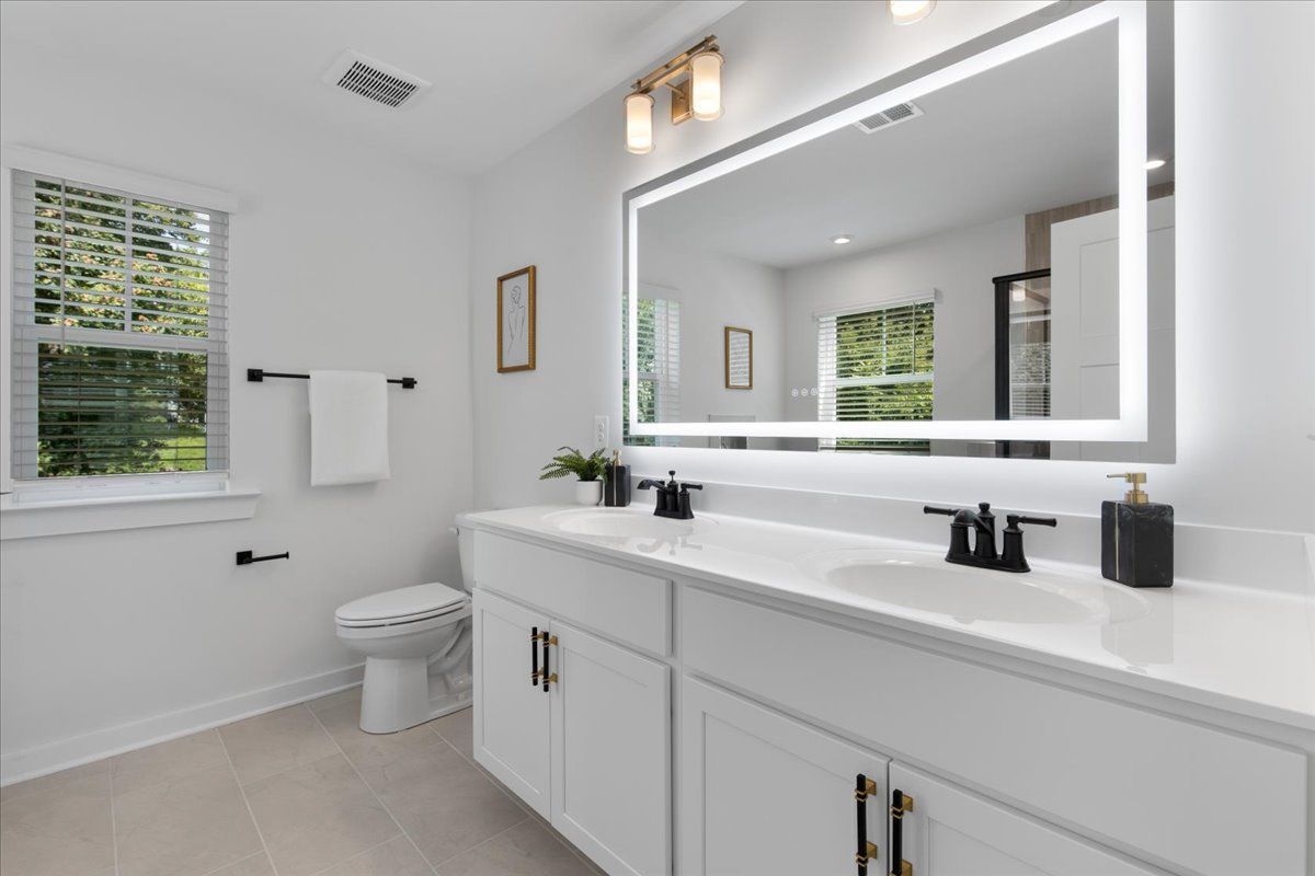 A bathroom with a toilet , sink , mirror and window.