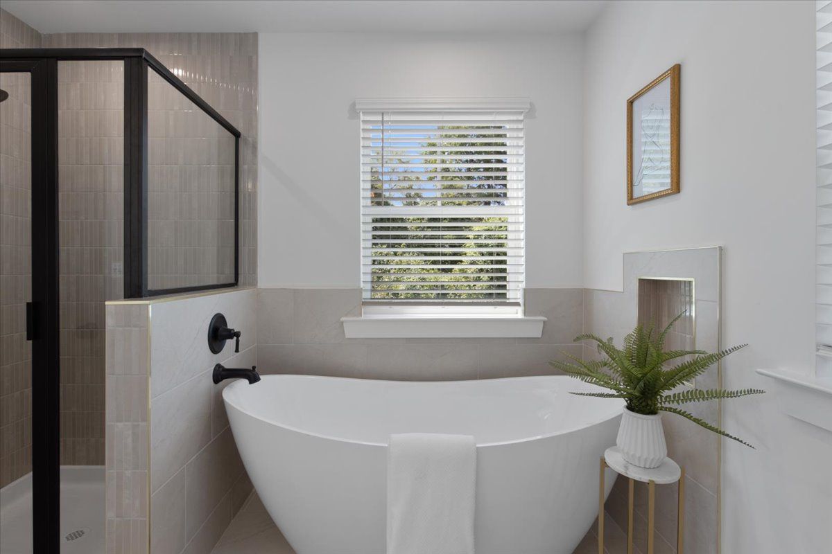 A bathroom with a tub , shower , mirror and window.