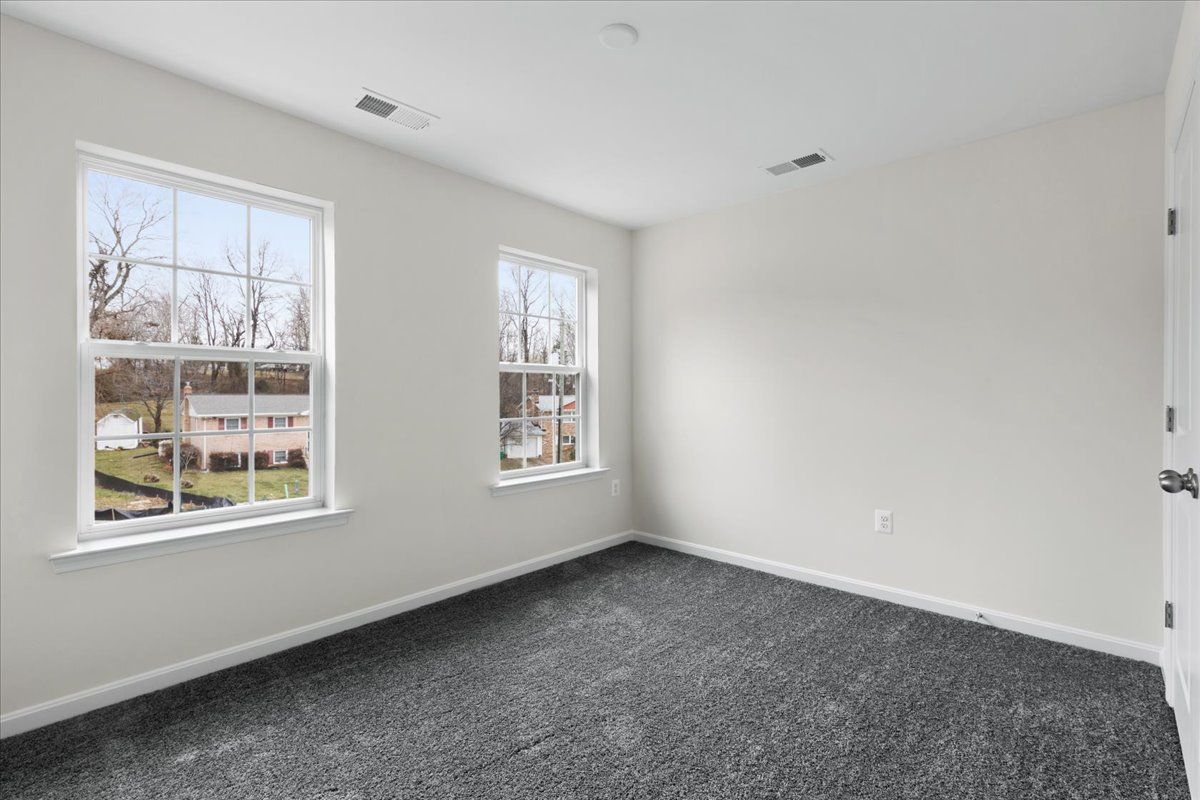 An empty bedroom with two windows and a gray carpet.