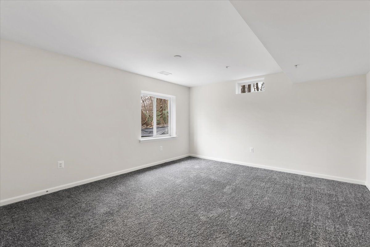 An empty room with a window and a gray carpet.