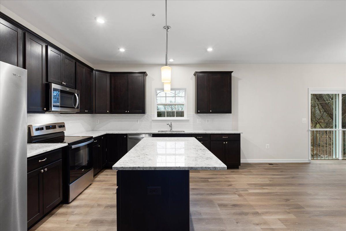 A kitchen with black cabinets and stainless steel appliances and a large island in the middle.
