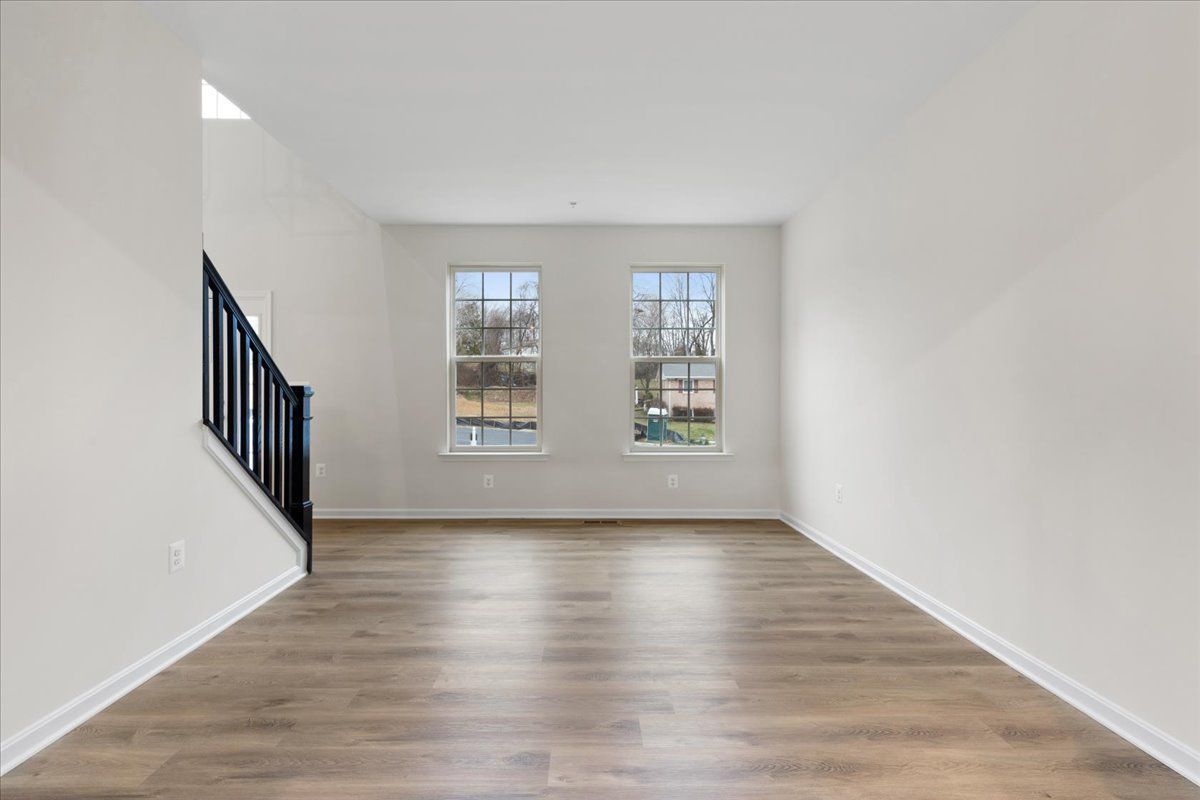 An empty living room with hardwood floors and two windows.