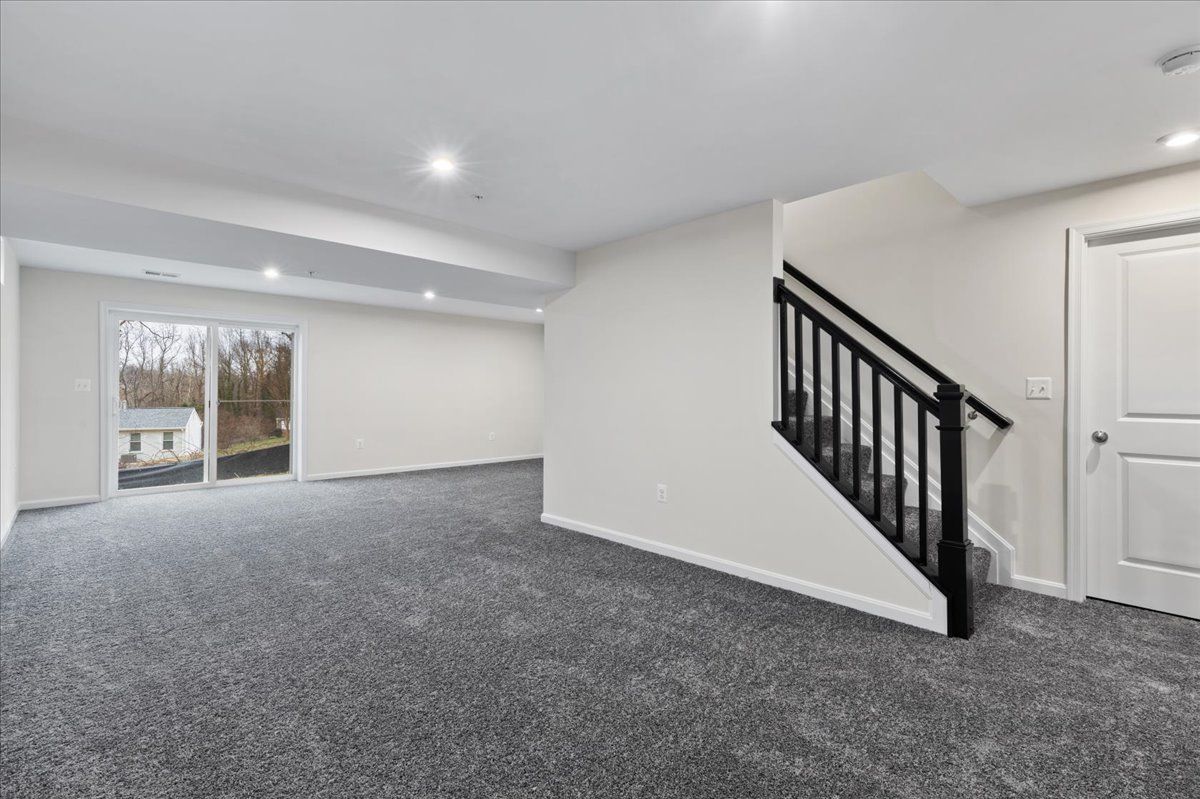 An empty basement with a staircase and sliding glass doors.