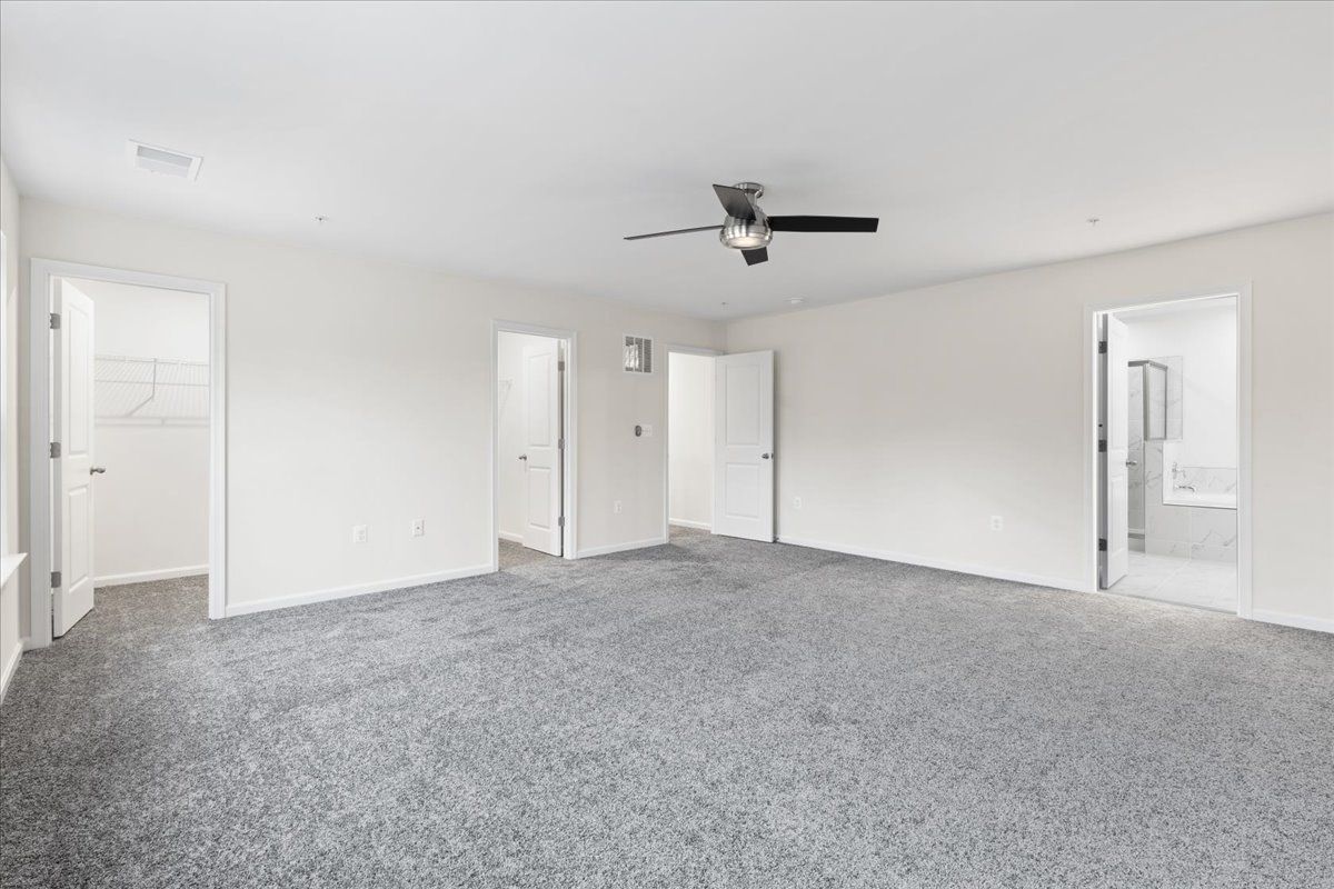A large empty room with a ceiling fan and a gray carpet.
