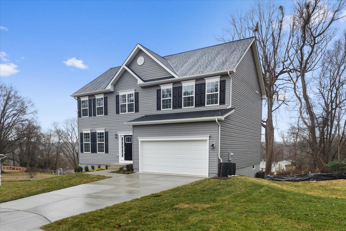 A large gray house with a white garage door is for sale.