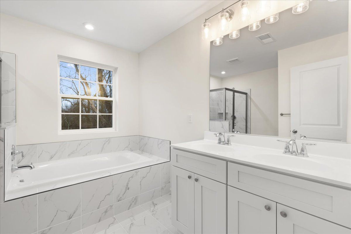 A bathroom with a tub , sink , mirror and window.