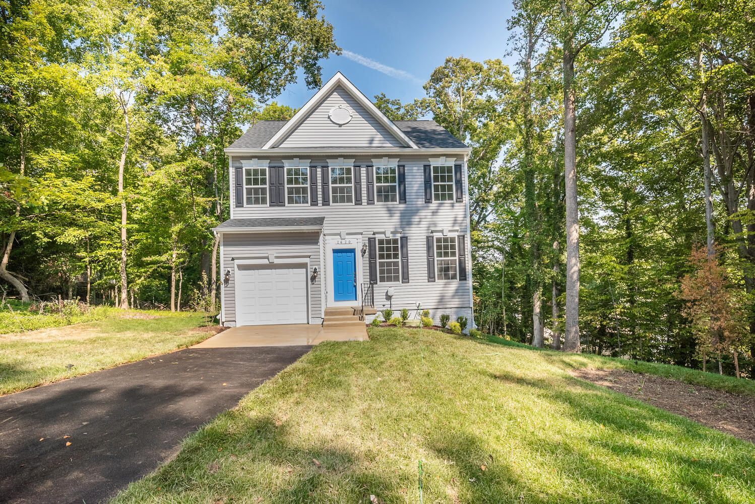 A white house with a blue door is surrounded by trees and grass.