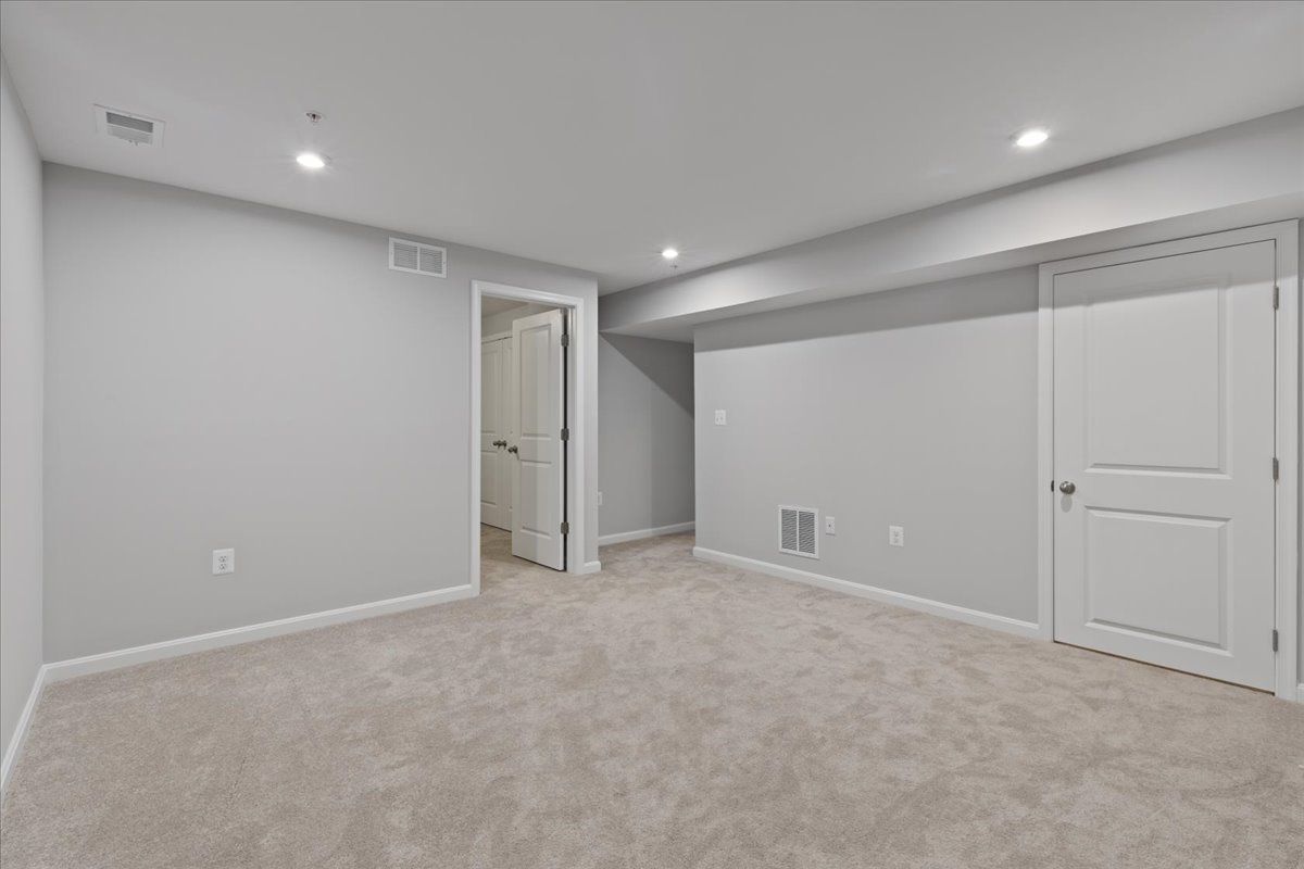 An empty basement with a carpeted floor and white walls.