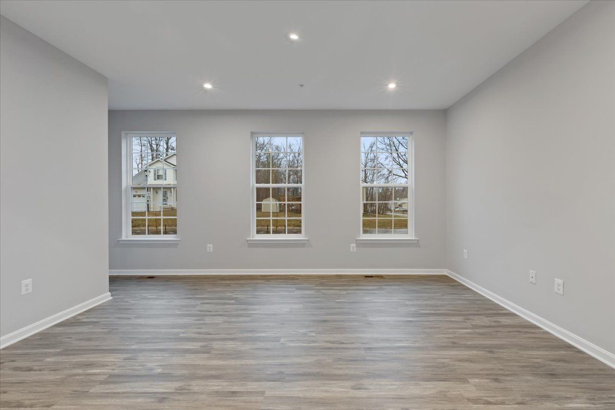 An empty room with hardwood floors and three windows.