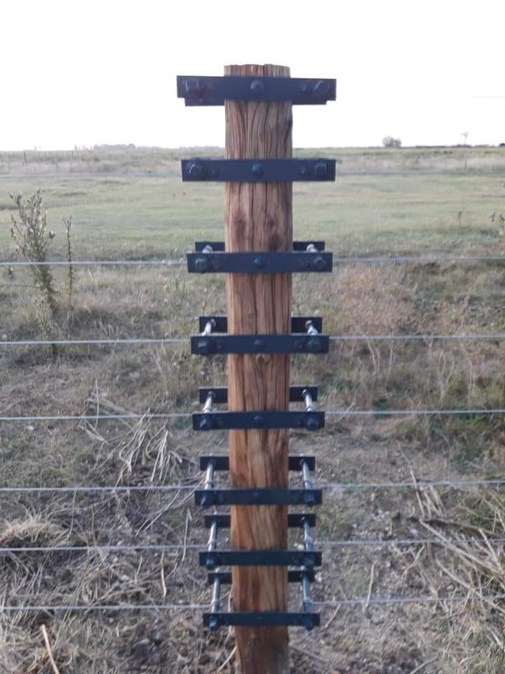 Poste de cerca de madera con soportes de metal que sostienen una cerca de alambre horizontal.