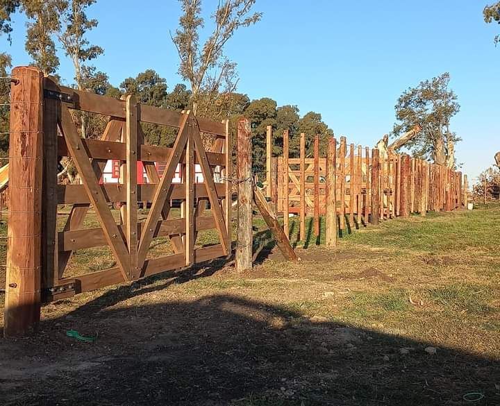 Valla y puerta de madera en un campo de hierba bajo un cielo azul claro.