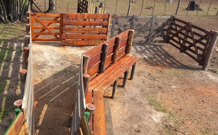 Corral de madera con portones y banco en entorno exterior.