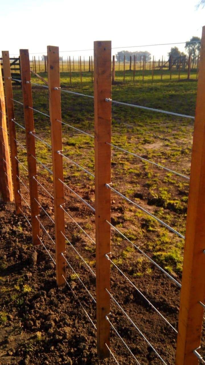 Poste de madera y valla de alambre en un campo, construido al aire libre.