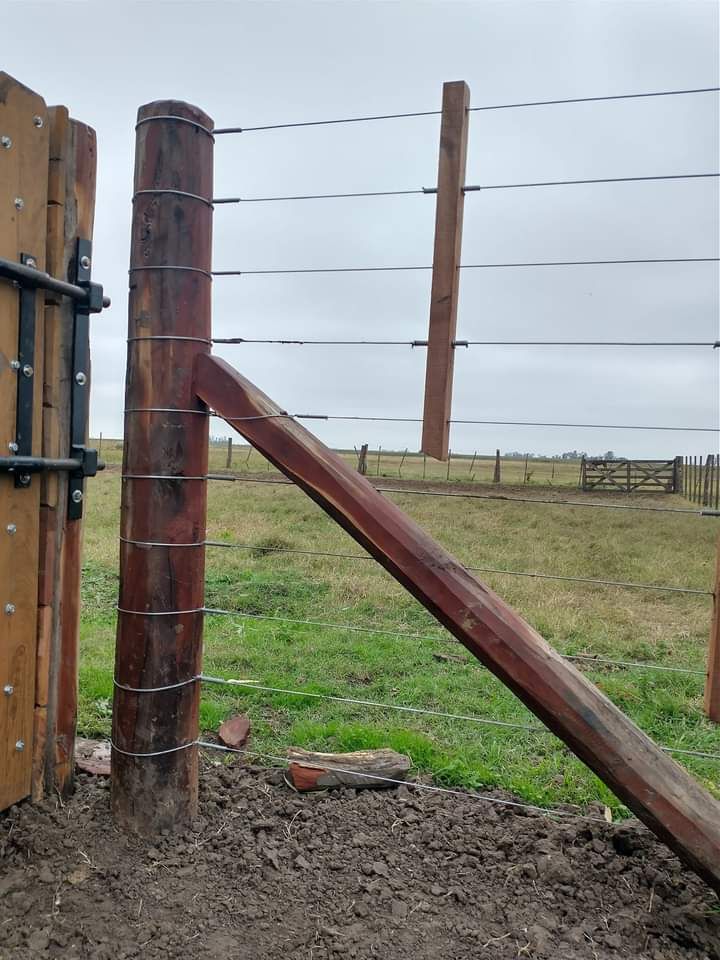 Poste de cerca de madera con viga de soporte, hilos de alambre y puerta en un campo de hierba.