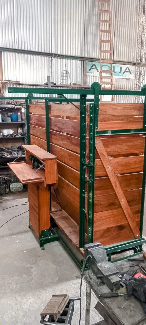 Estructura construida en madera y color verde en un taller, con una pequeña mesa adjunta a la izquierda.