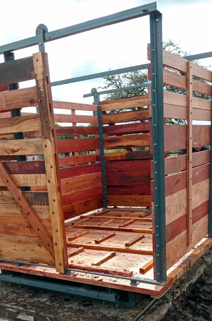 Establo de madera y metal para animales en construcción al aire libre. Estructura de madera marrón rojiza y metal gris.