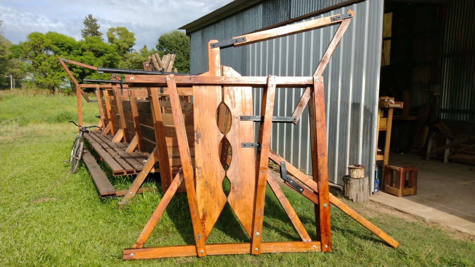 Ganado de madera aplastado en un campo de hierba frente a un cobertizo de metal corrugado.
