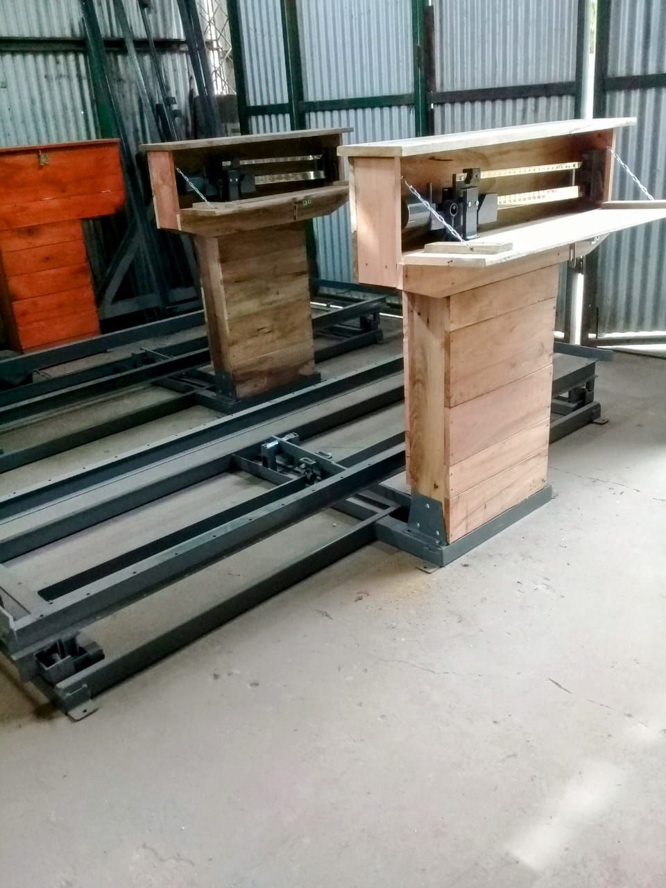 Dos podios de madera sobre raíles metálicos, en el interior de un taller con paredes de chapa ondulada.