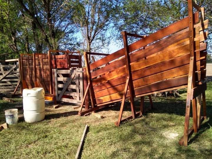 Corral de madera para ganado en construcción sobre un campo de hierba, con madera marrón y vigas de soporte.