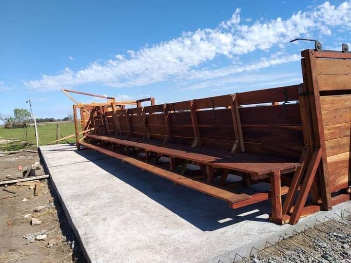 Conducto de madera para ganado sobre una base de hormigón al aire libre bajo un cielo azul.