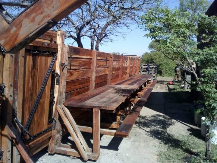 Banco de madera para exterior con mesa larga, pared de madera y un entorno exterior soleado.