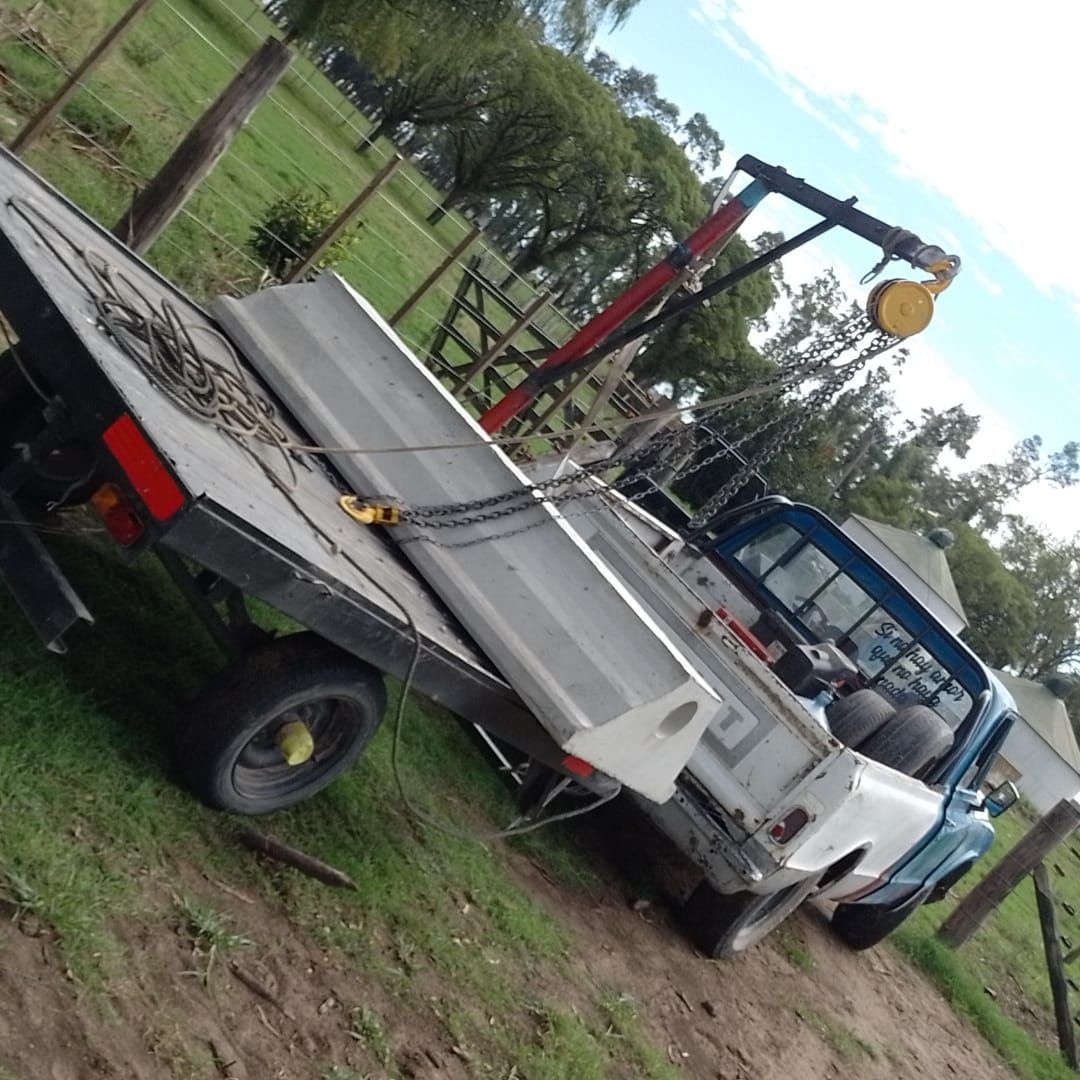 Camión de plataforma que transporta un objeto de hormigón en un campo. Lleva una grúa acoplada.