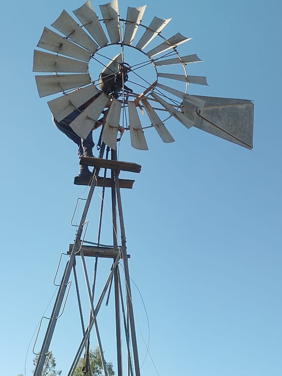 Molino de viento contra un cielo azul despejado. Aspas metálicas y estructura de soporte.