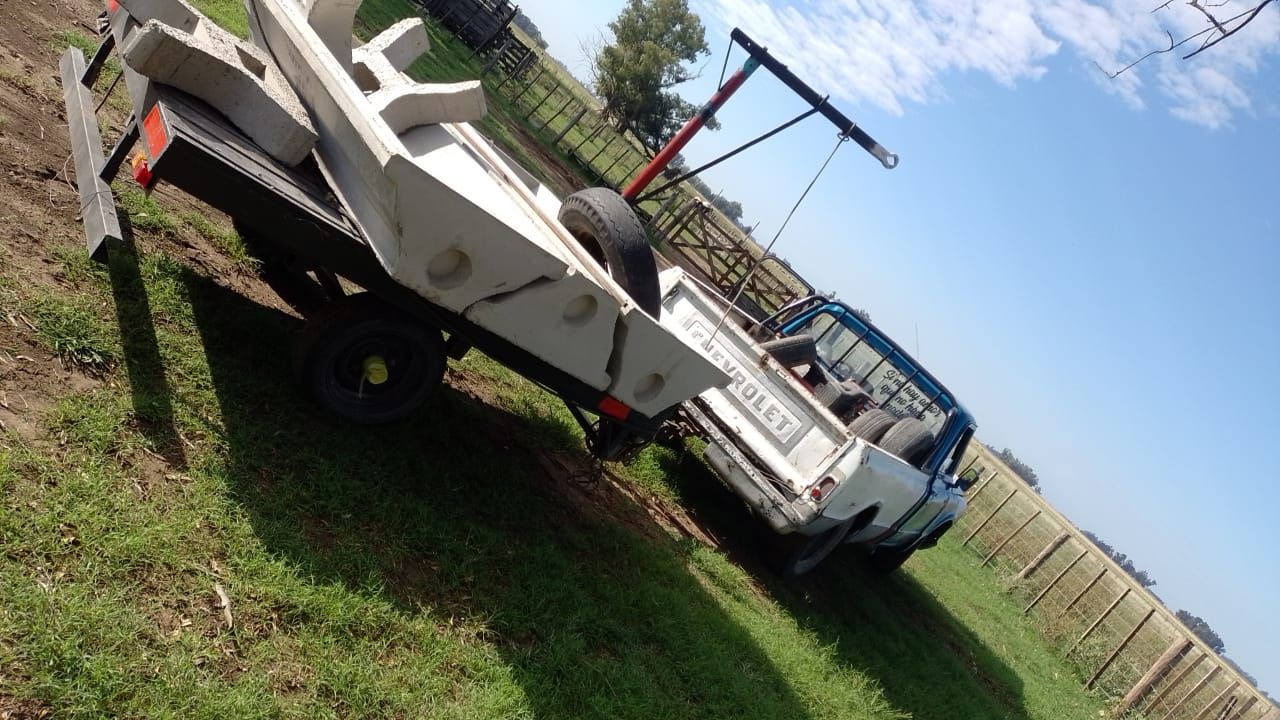 Un barco en un remolque enganchado a una camioneta blanca en un campo de hierba bajo un cielo azul.