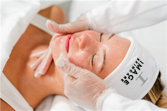 Woman receiving facial treatment, hands on face, wearing headband, in a spa setting.