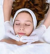 Person getting a facial treatment with gloved hands, eyes closed, white headband.