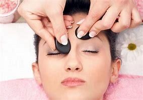 Woman receiving hot stone facial massage, eyes closed, in a spa setting.