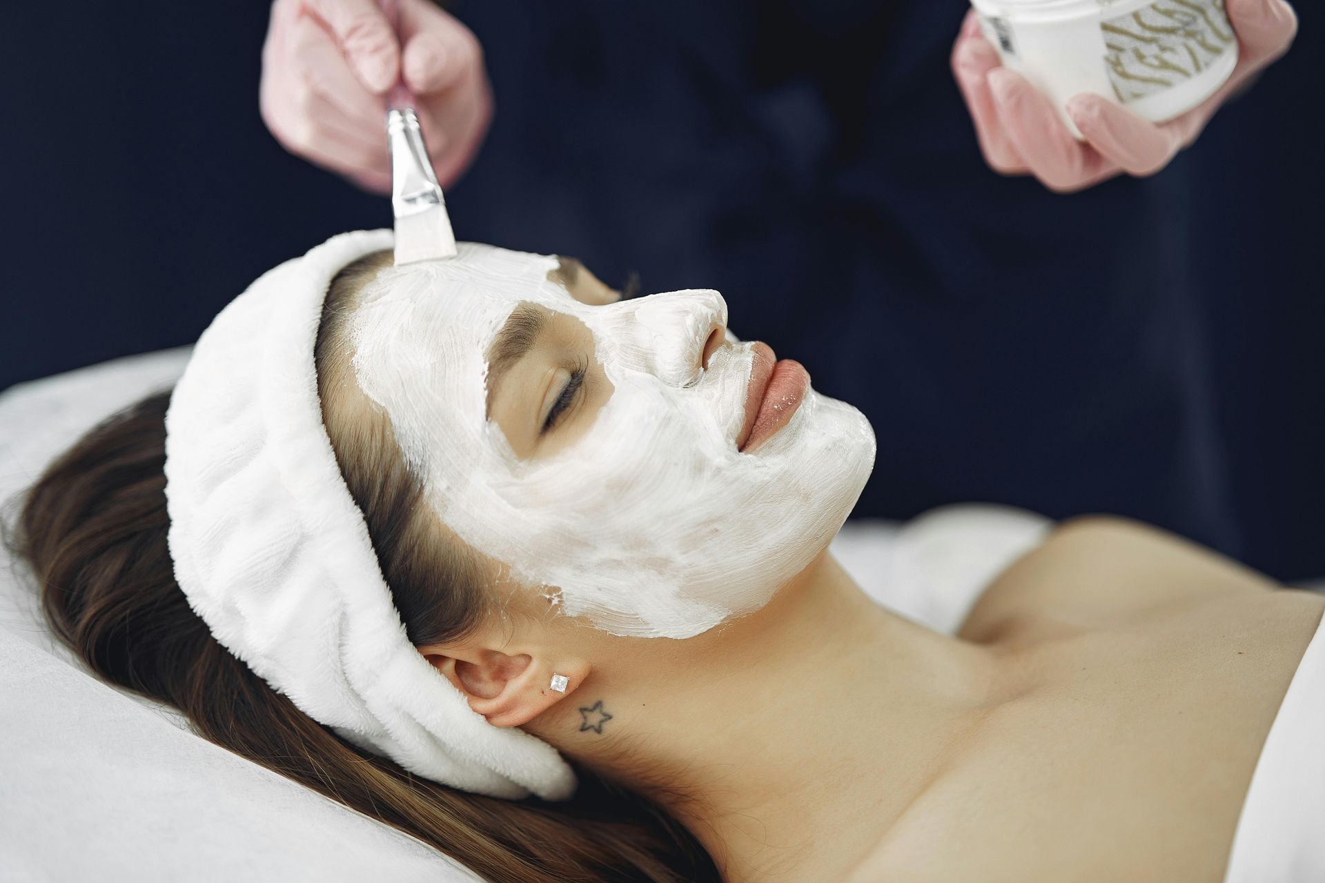 Woman with closed eyes, green facial mask, being treated with brush at a spa.