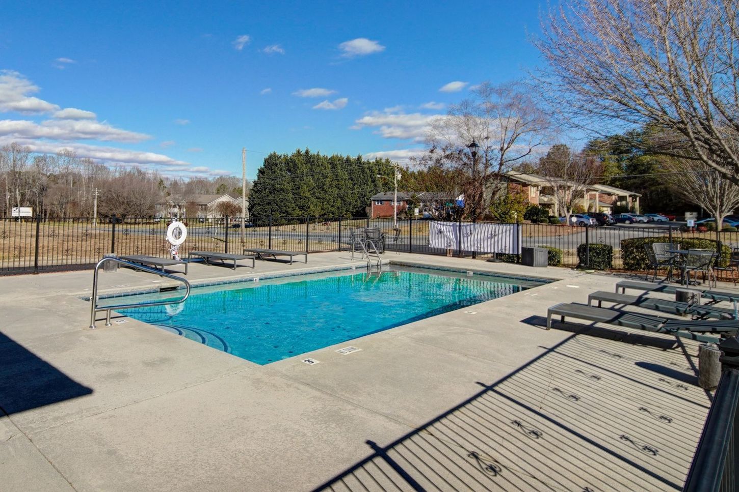 A large swimming pool surrounded by a fence and chairs on a sunny day.