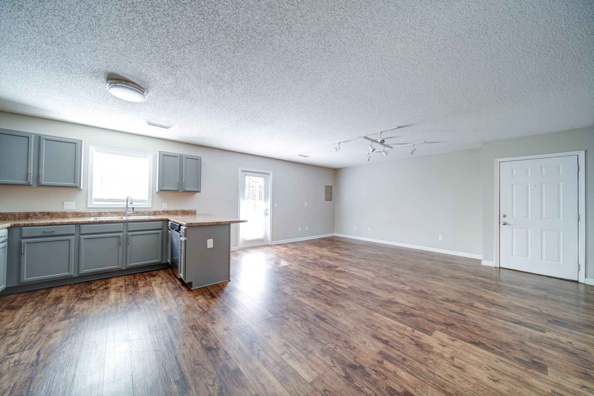 A large empty room with hardwood floors and a kitchen.