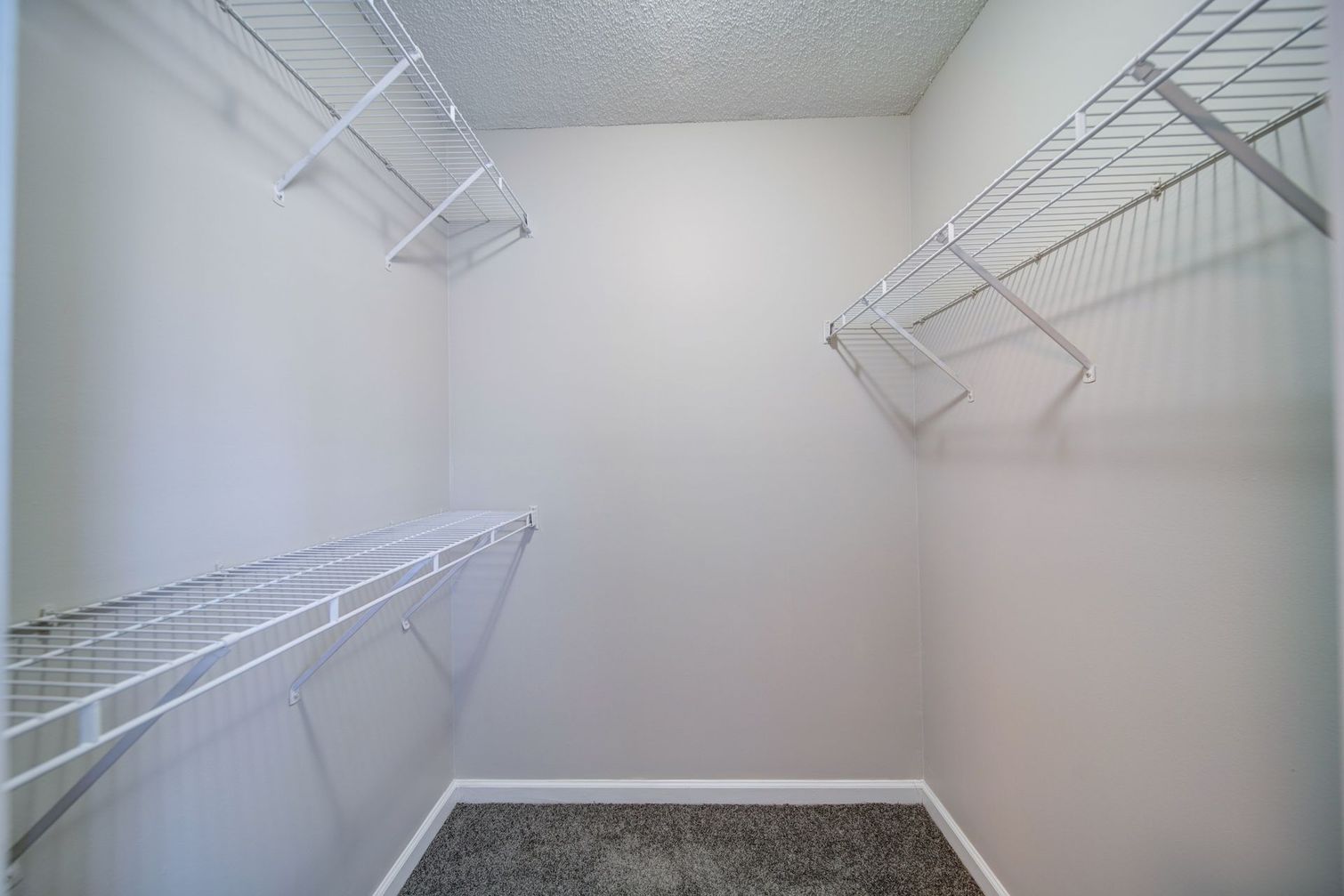 An empty walk in closet with wire shelves and a carpeted floor.