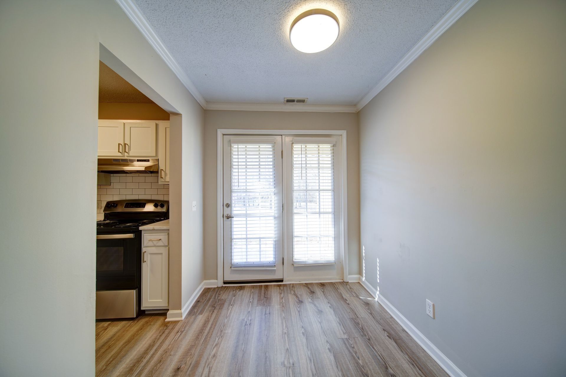 A living room with hardwood floors and a sliding glass door leading to a kitchen.