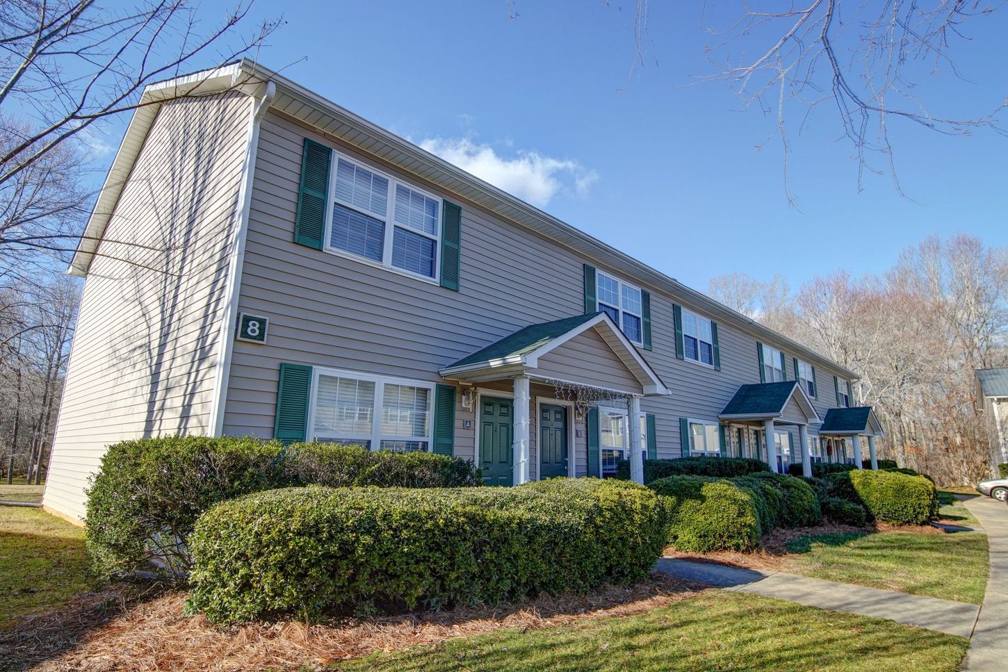 A large apartment building with green shutters and bushes in front of it.