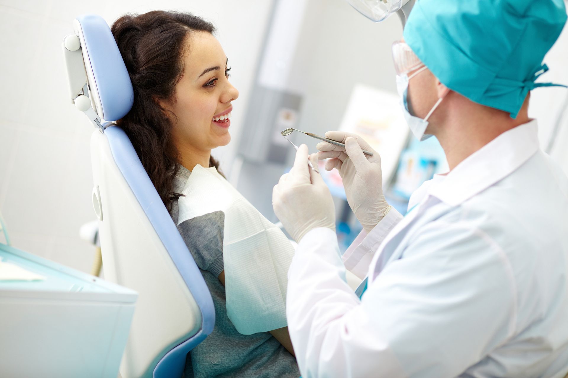 A woman is sitting in a dental chair while a dentist examines her teeth.