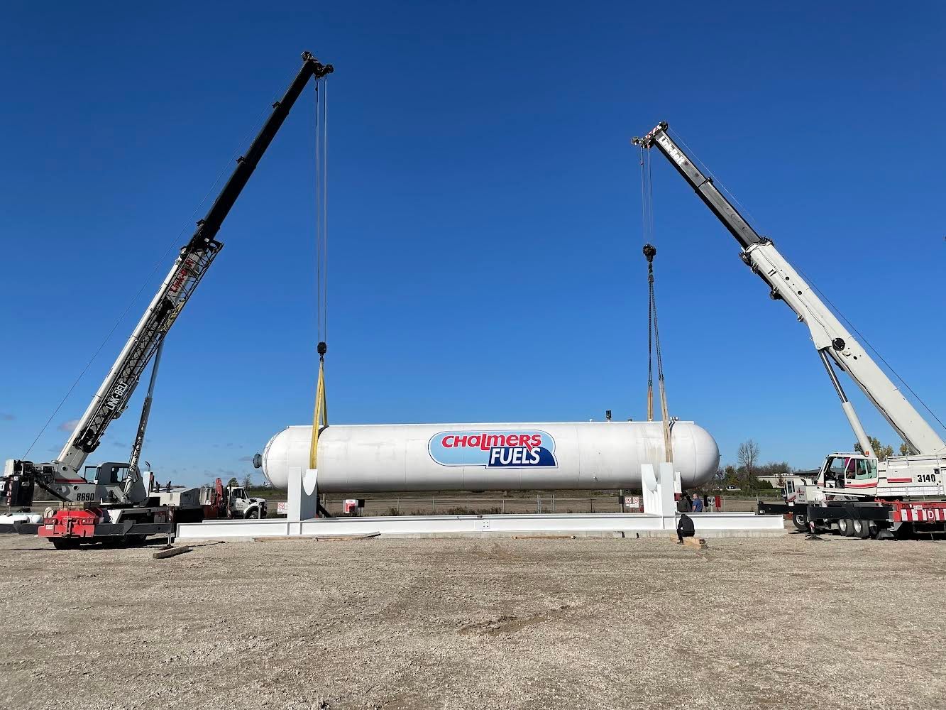 A large propane tank is being lifted by two cranes