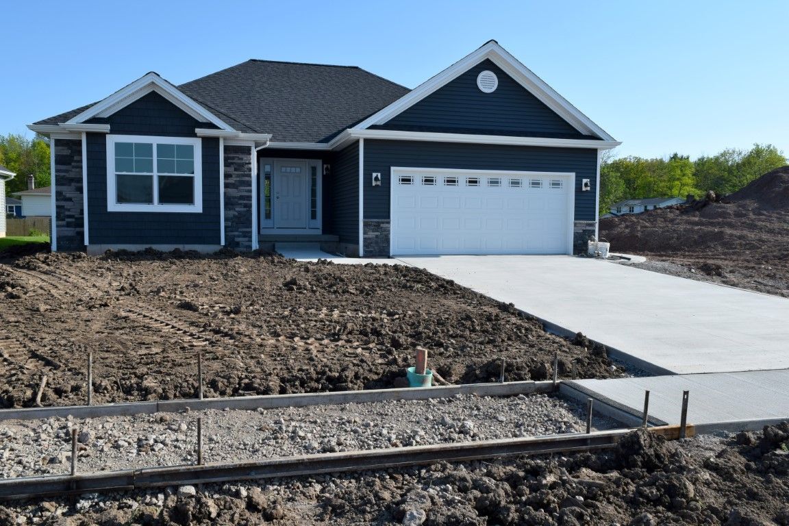 Single-story house with blue siding, white trim, and a garage, under construction with a dirt yard and concrete driveway