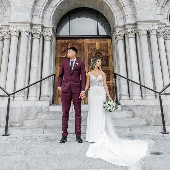 A bride and groom are standing in front of a building holding hands.