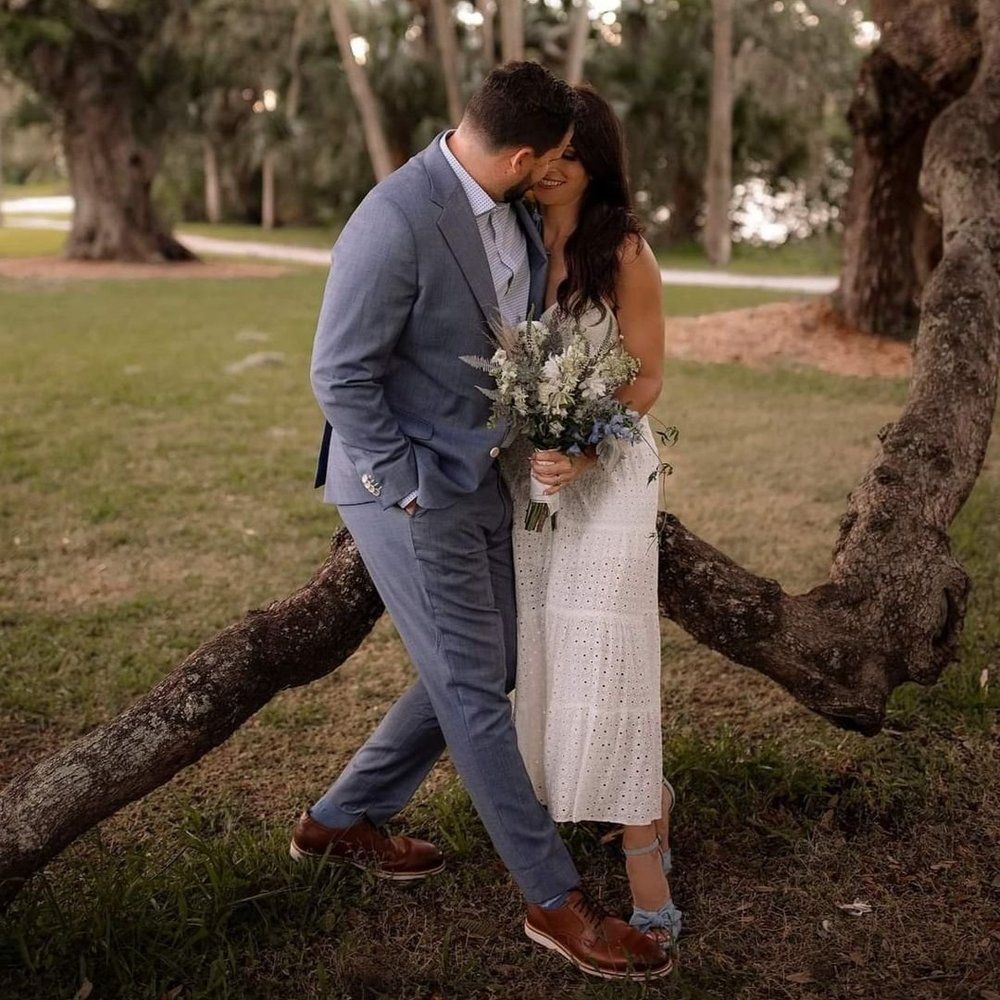 A bride and groom are kissing while leaning against a tree branch.