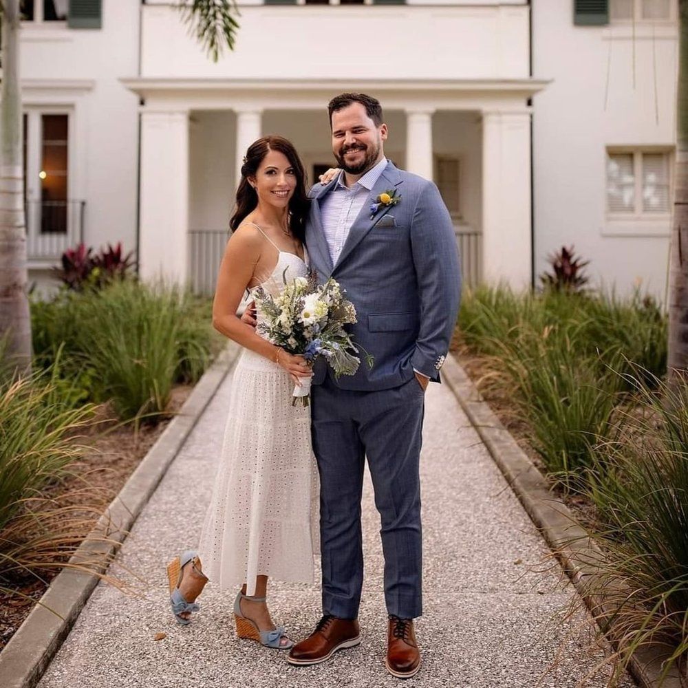 A bride and groom are posing for a picture in front of a white building.