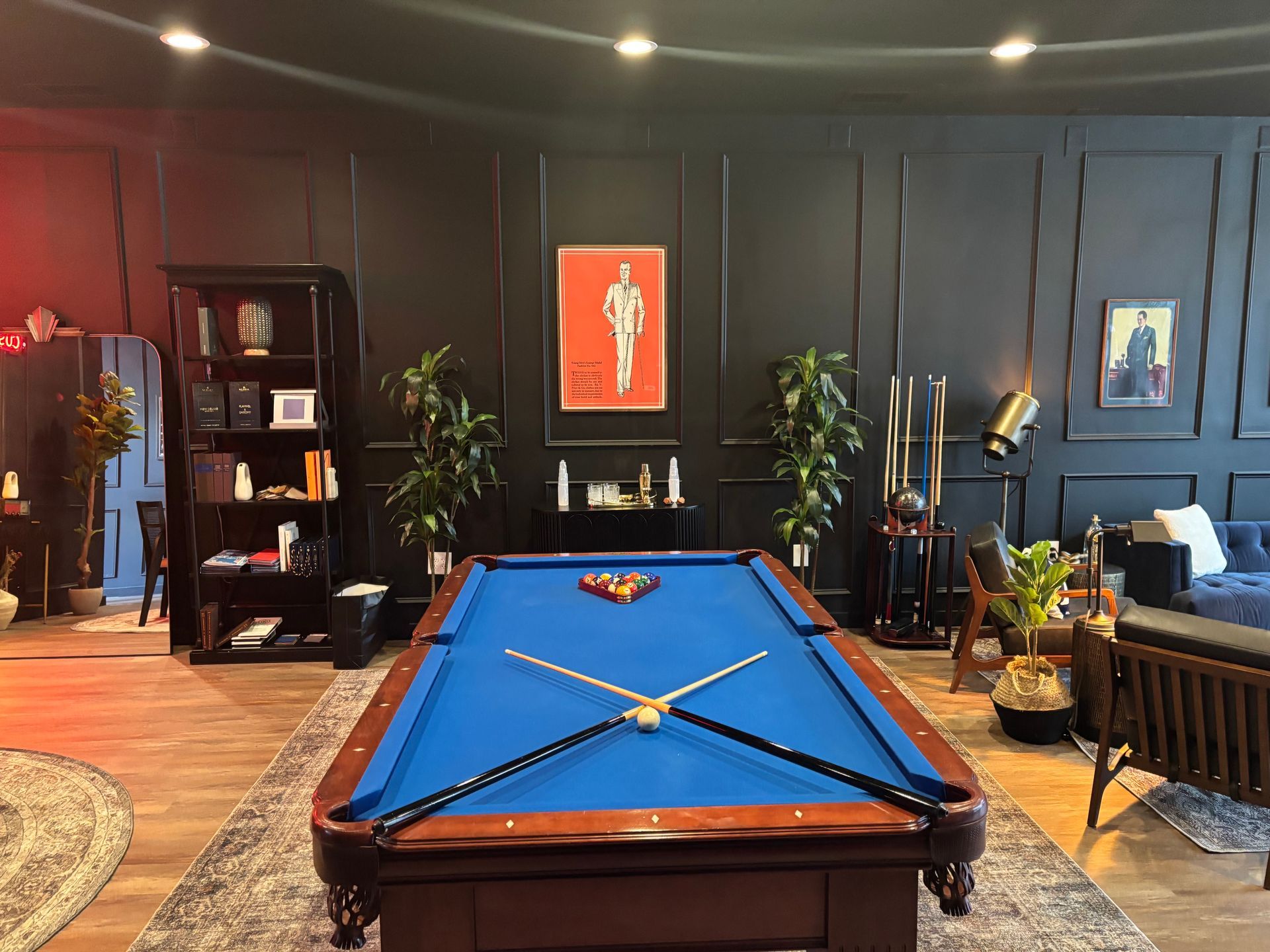 Pool table in a dark room with plants, art, and a black bookshelf.