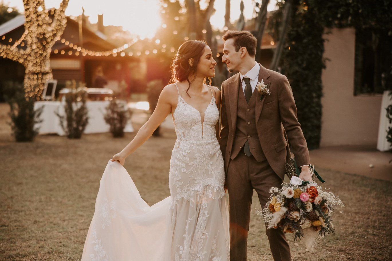 A bride and groom are standing next to each other in a field holding a bouquet of flowers.