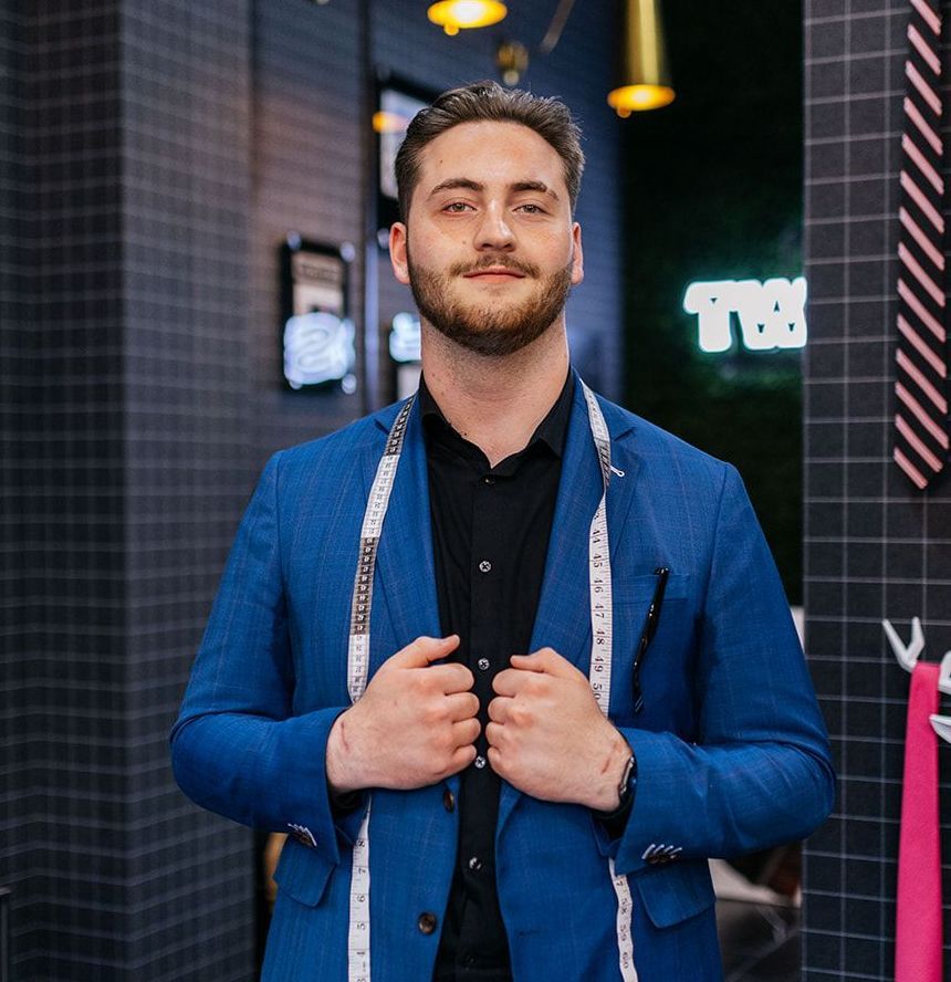 A man in a blue suit with a measuring tape around his neck