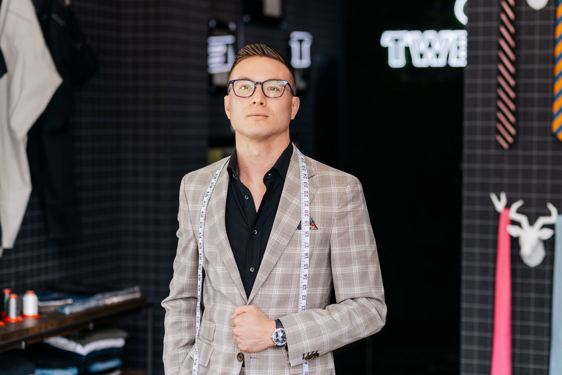 A man in a suit is standing in a room with a measuring tape around his neck.